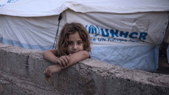 Åtta-åriga Raghda Abbas Suleiman tittar ut över en mur nära familjens tält i Bardarash-lägret i Duhok, Irak, dagen efter att hon anlände med sin familj.  UNHCR skyddar människor som flyr strider i norra Syrien. Familjer får hjälp med tält och filtar och andra förnödenheter för att överleva.