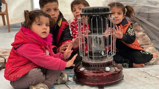 Barn på flykt från Syrien värmer händerna över en kamin i ett tältläger i Irak.