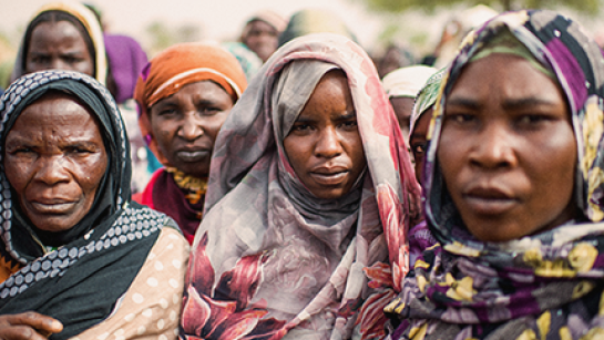 Tre kvinnor i närbild som flyr från Sudan tittar in i kameran.