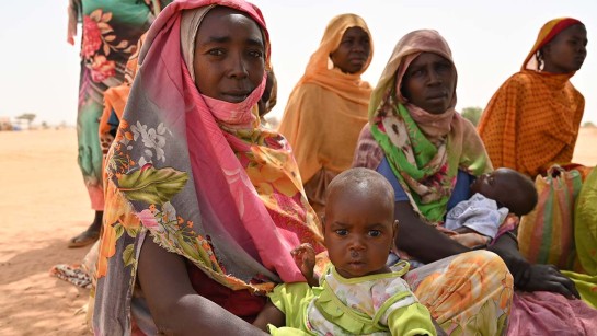 Kvinnor och barn på flykt från Sudan sitter på sanden i Chad.