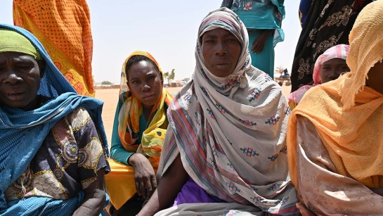 Kvinnor på flykt från Sudan sitter i sanden i Tchad.