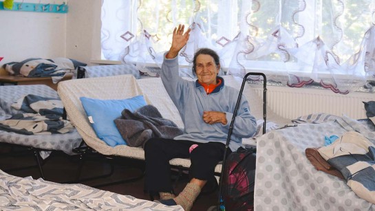 Baba Nina vinkar från sovsalen där hon har fått skydd och hjälp.