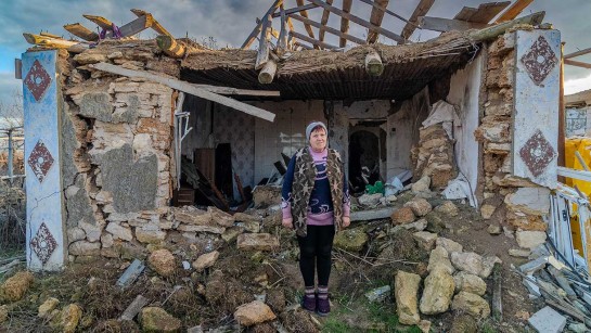 En kvinna står utanför sitt sönderbombade hem i Ukraina.