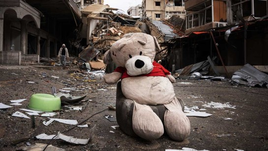 En nallebjörn sitter på en soffa framför en sönderbombad byggnad i södra Libanon.