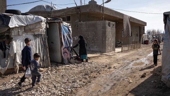 Tre syriska flyktingbarn går på en lerig väg i ett tältläger i Libanon.