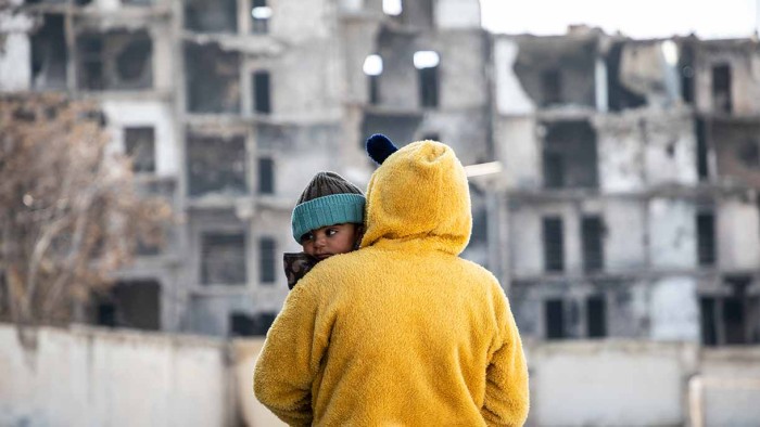 En flicka bär sin lillasyster på en skolgård i Aleppo. Skolan används just nu som sovsal för familjer som är drabbade av förödande jordbävningar.